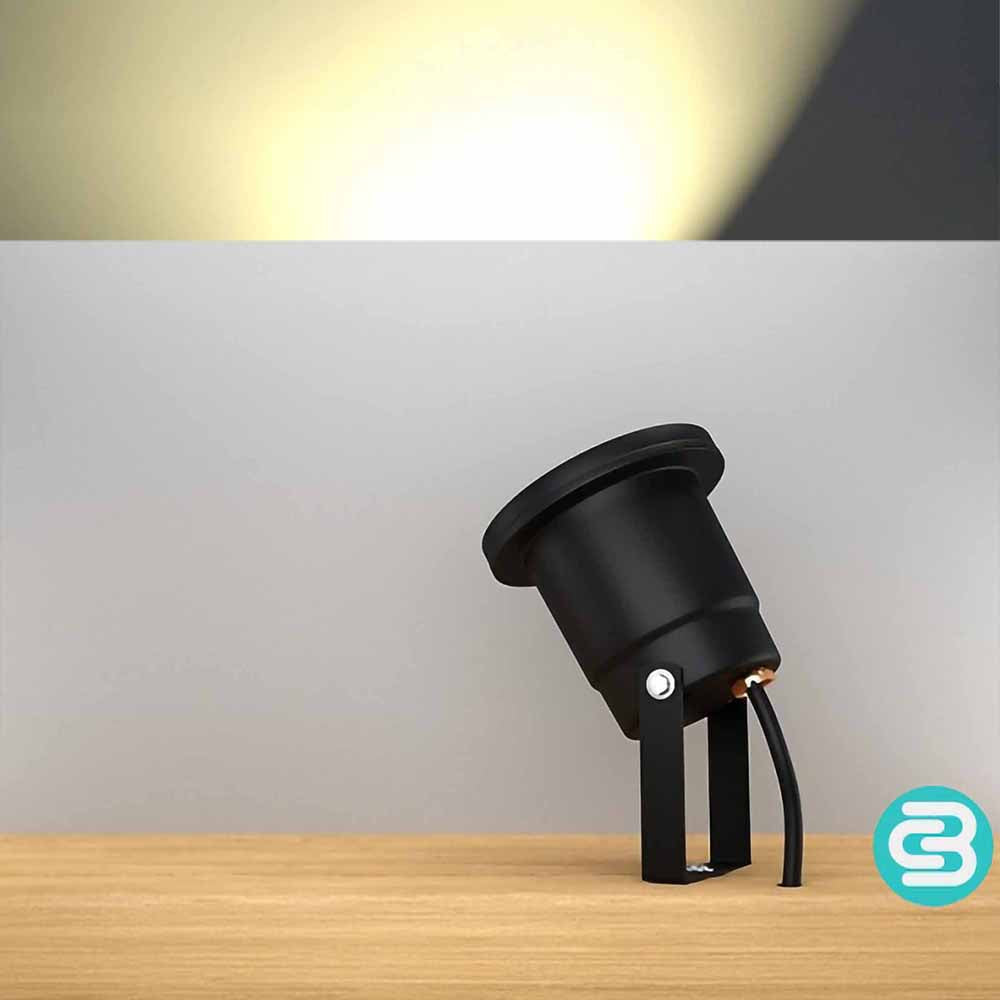 Black outdoor light fixture on a wooden surface with a warm white LED light on a gray background.