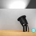 Black outdoor light fixture on a wooden surface with a white LED light on a gray background.